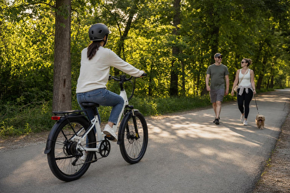 FavoriteBikes step-through electric bike on a paved multi-use shared trail in a wooded city park, with a calm rider slowing down to pass two pedestrians and a leashed dog on the left at a polite distance