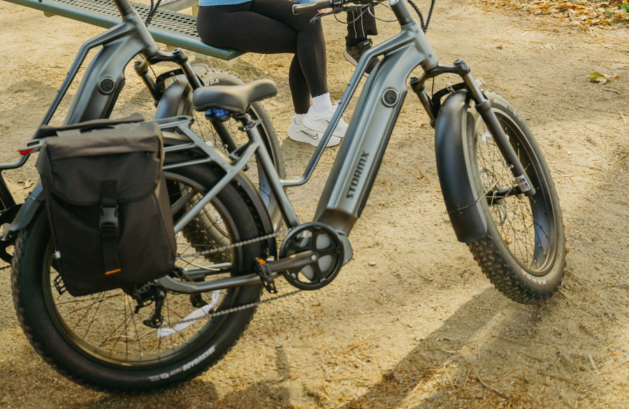 Black pannier beside the rear wheel of a gray STORMX e-bike, with the rack platform visible above it.