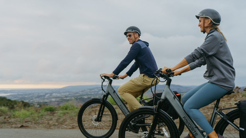 Two helmeted FavoriteBikes riders riding together on a coastal road