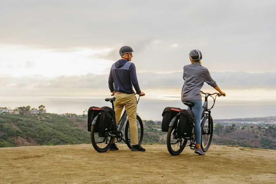 Two people with dark bicycles overlooking hills, wearing navy, mustard, gray and blue.
