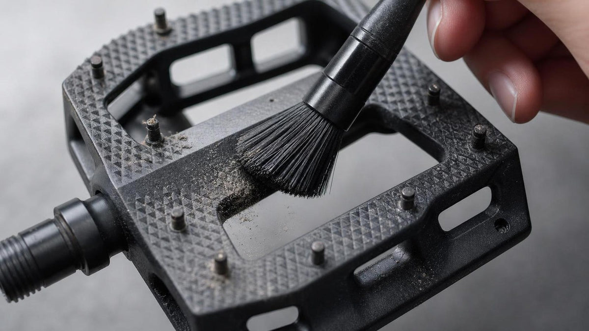 Close-up of an e-bike flat platform pedal being cleaned with a brush, showing the textured grip surface and grip pins