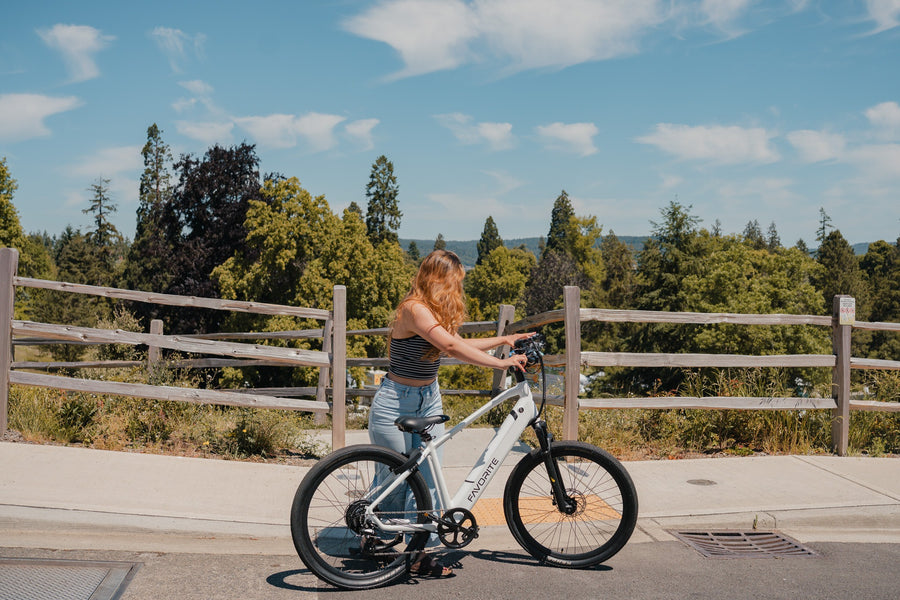 Person in a striped black top and light blue jeans standing beside a white FAVORITE bicycle at a wooden fence.