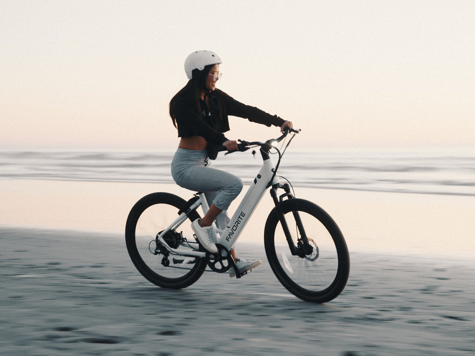 Rider on a white FavoriteBikes electric bike along a calm beach at sunset