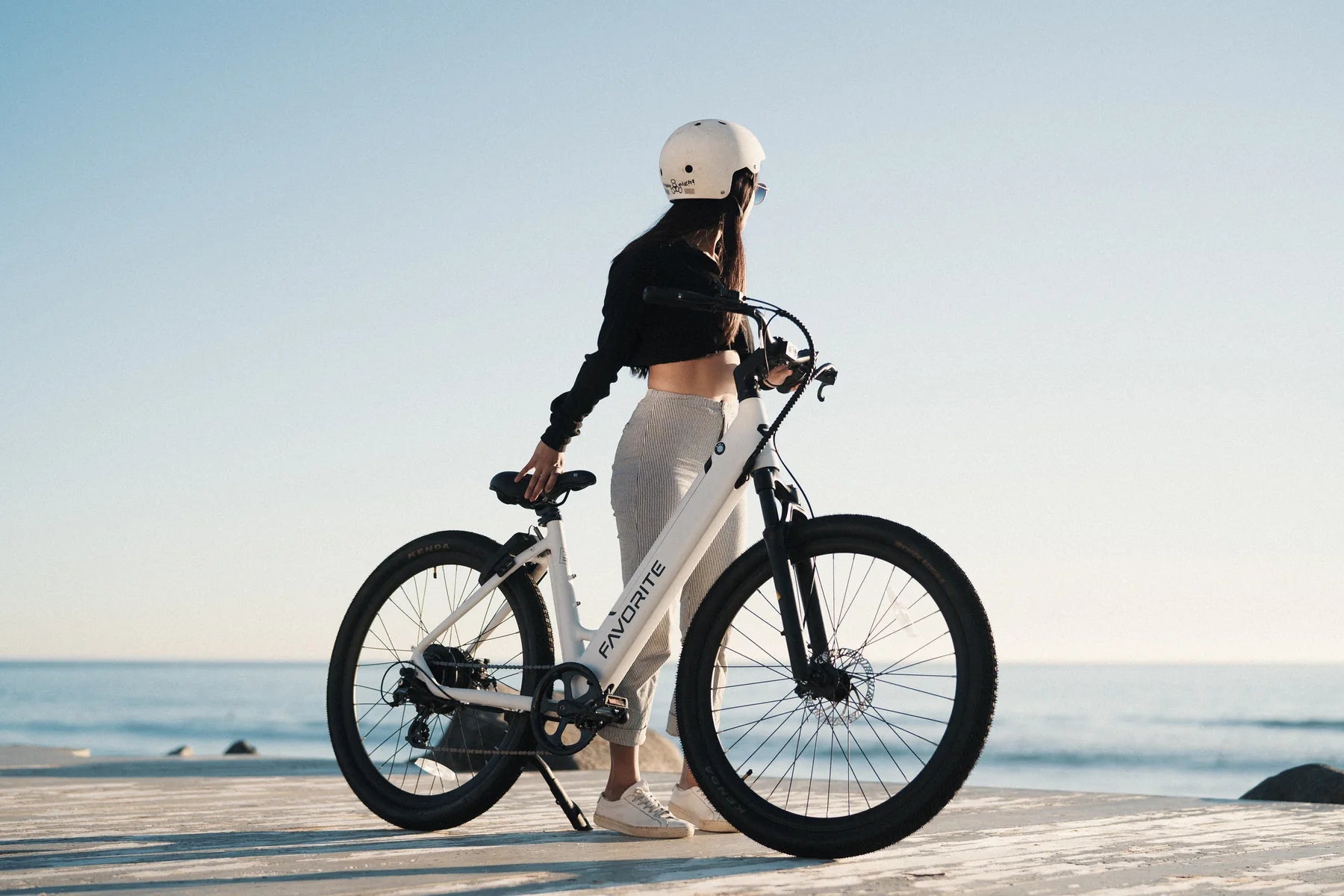 Woman standing with a white FavoriteBikes Hybrid ST electric bike beside the ocean