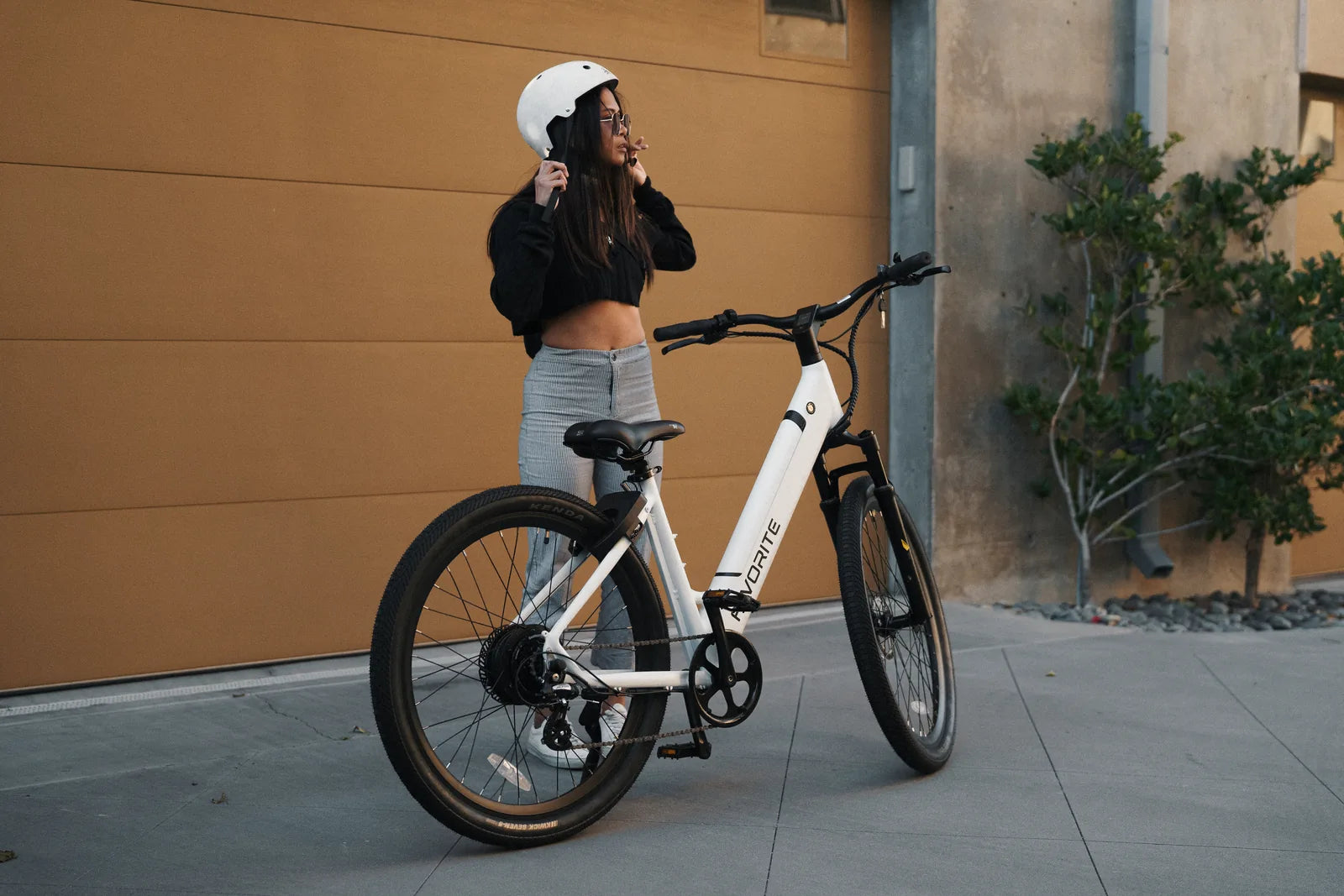 Woman adjusting her helmet beside a white FavoriteBikes Hybrid ST electric bike